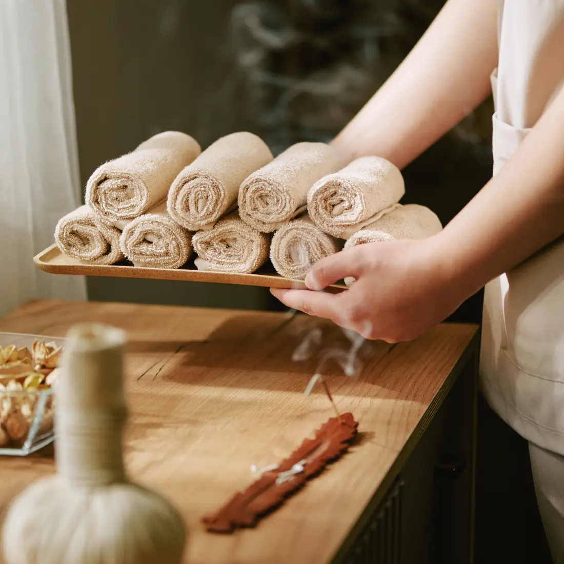 spa attendant holding rolled towels and incense