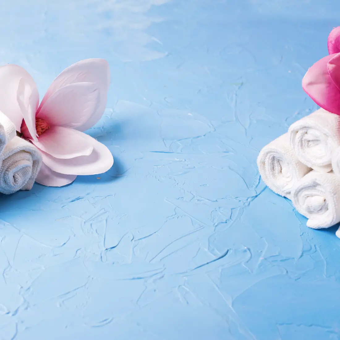 rolled white towels and pink magnolia flowers on blue