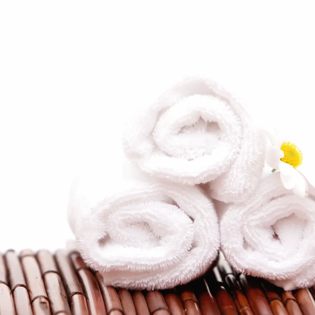 rolled white towels with a daisy on bamboo mat