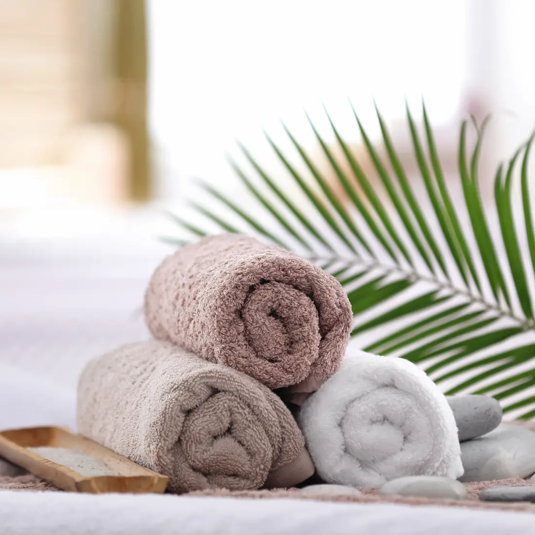 rolled towels, stones, and palm frond on a spa bed