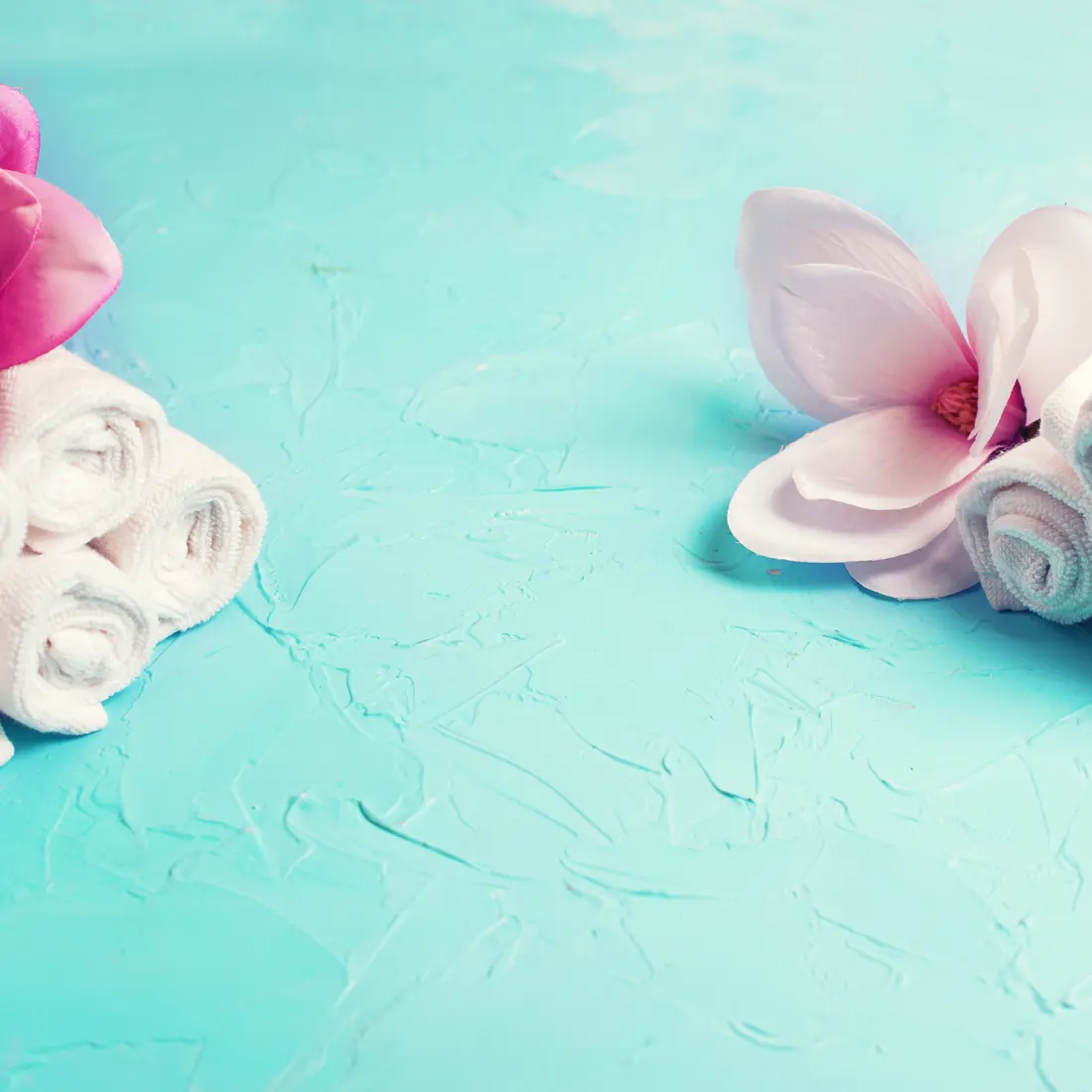rolled towels and magnolia flowers on blue background