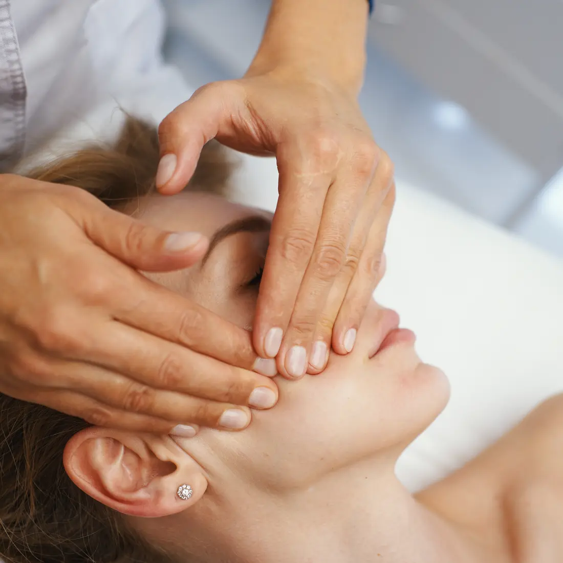 hands massaging woman's face during facial treatment