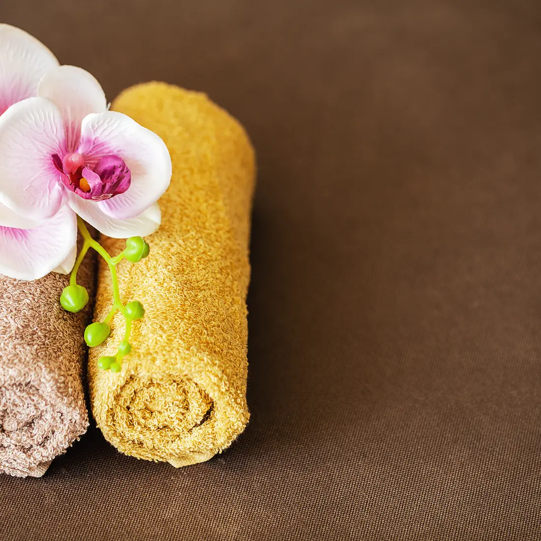 rolled towels with orchid flowers on brown background