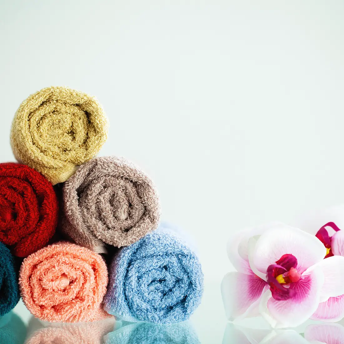 rolled towels and orchids on reflective surface