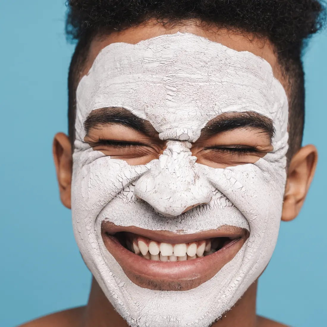 man with white clay face mask smiling