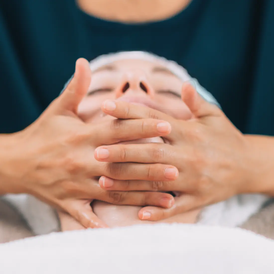 hands massaging a woman's face during facial treatment